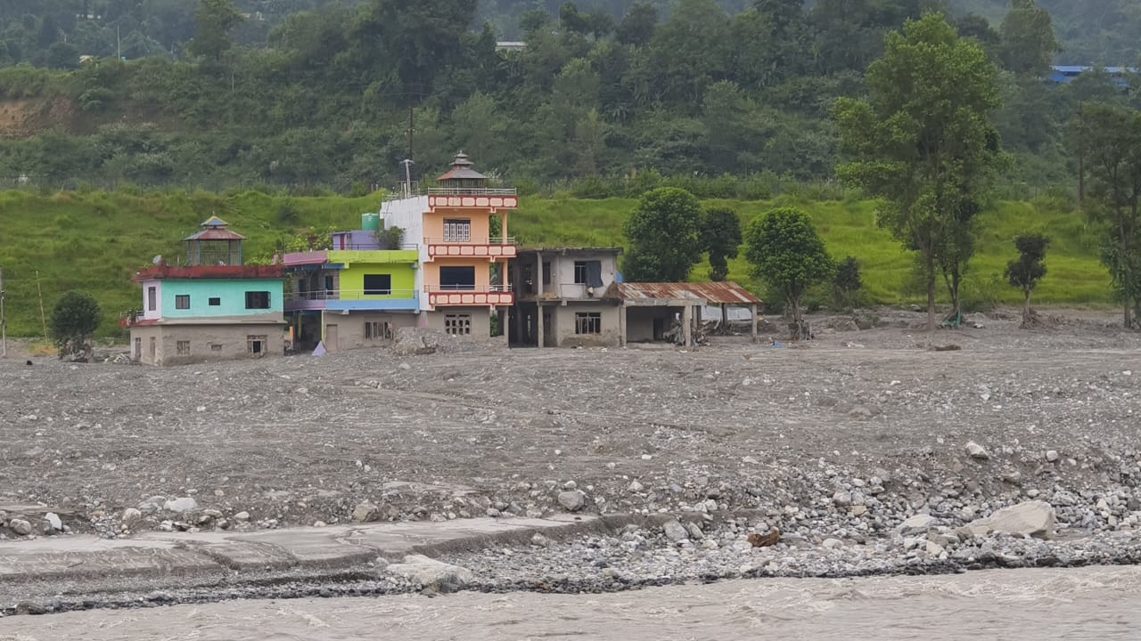 Painted houses standing above a wide plain of grey silt beside the river