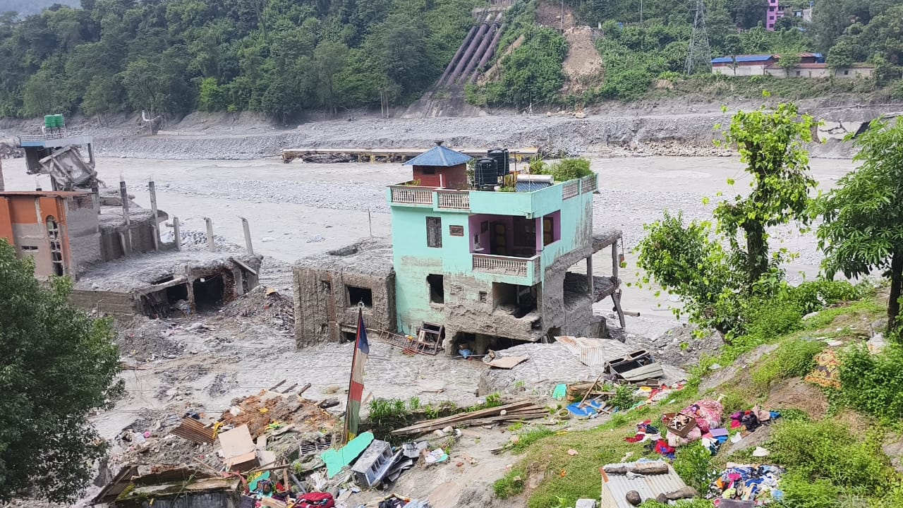 A green house left at the edge of the riverbank with debris scattered around it