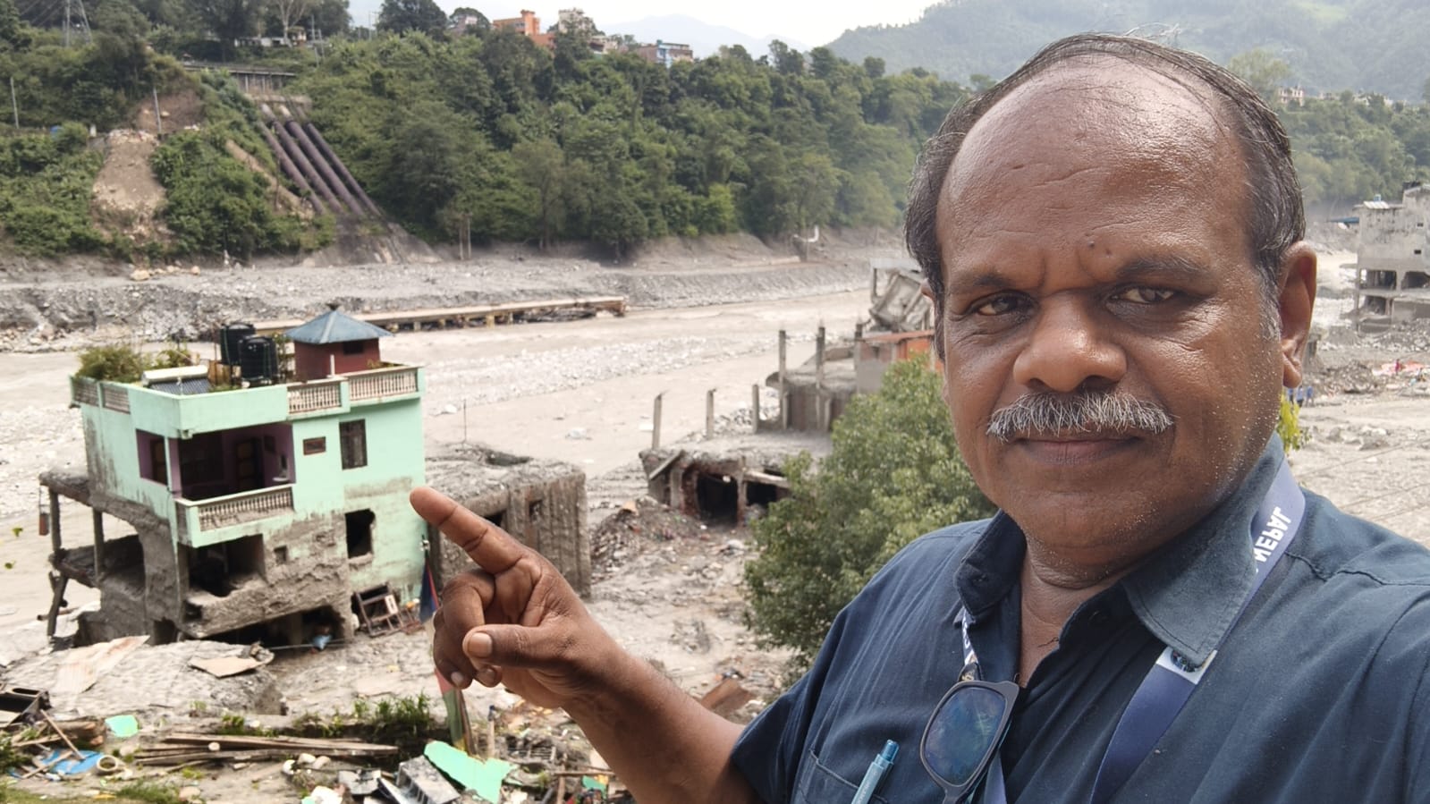 A Cry for Nepal team member at the site, pointing towards a silt-covered house