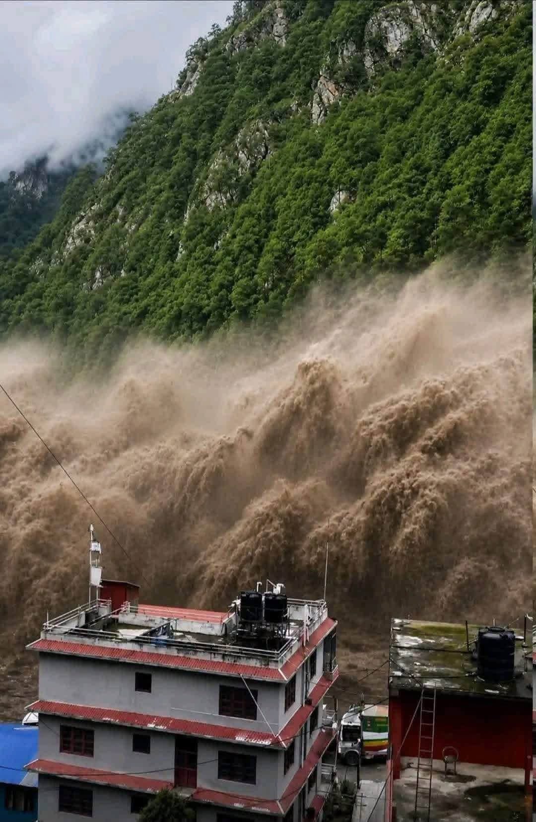 A wall of floodwater and debris surging down the hillside behind homes in Rasuwa